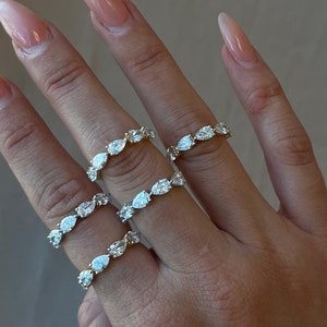 May include: A hand wearing four gold rings with pear-shaped clear stones. The rings are stacked on each other.