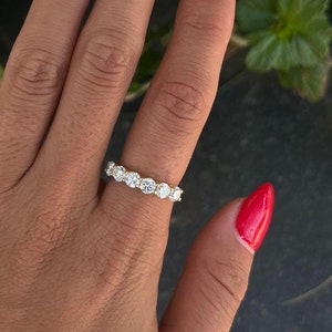 May include: A hand with red nail polish is wearing a gold band ring with a row of clear round stones.