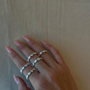 May include: Three gold rings with pear-shaped clear stones set in a continuous line around the band.