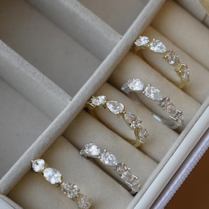 May include: A white velvet-lined jewelry box with six compartments, each containing a gold band with pear-shaped diamonds.