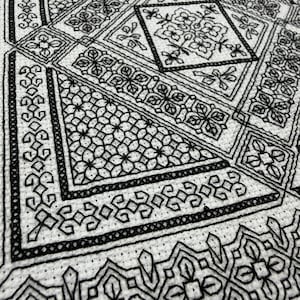 May include: A white fabric piece featuring intricate black embroidery in a geometric pattern. The design consists of repeating floral motifs, diamond shapes, and linear borders, all executed with precise black thread on a textured weave.
