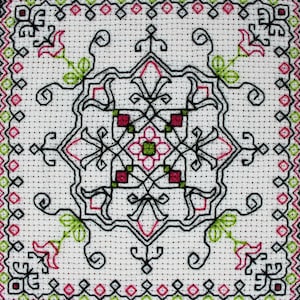May include: A white fabric with a black, green, and pink embroidered design. The design features a central square with four smaller squares in each corner. The design is symmetrical and intricate.