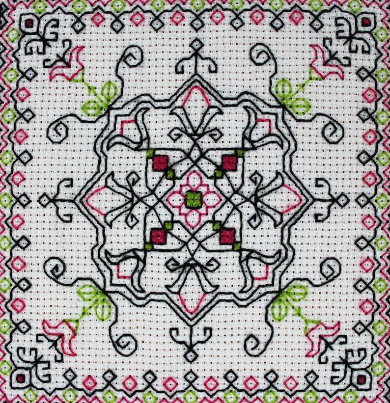 May include: A white fabric with a black, green, and pink embroidered design. The design features a central square with four smaller squares in each corner. The design is symmetrical and intricate.