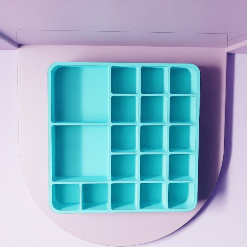 May include: A turquoise-colored organizer with multiple square compartments and two larger rectangular sections. The organizer is set against a light purple background with a curved, light pink accent.