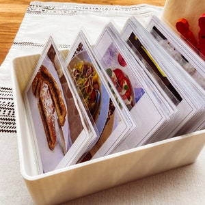 May include: A white plastic storage box filled with a stack of index cards. Each card features a close-up photograph of a different food item.