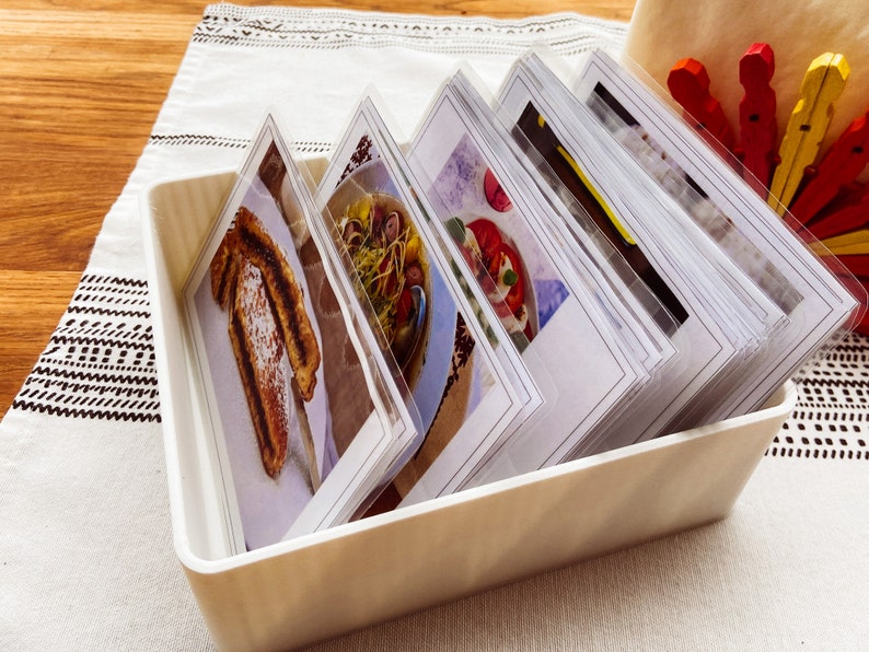 May include: A white plastic storage box filled with a stack of index cards. Each card features a close-up photograph of a different food item.