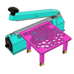 May include: A teal and black heat sealer with a pink honeycomb-patterned stand. The stand has four legs and is about 10 inches tall.
