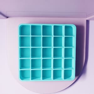 May include: A turquoise blue silicone mold with 25 square compartments. The mold is on a white surface.