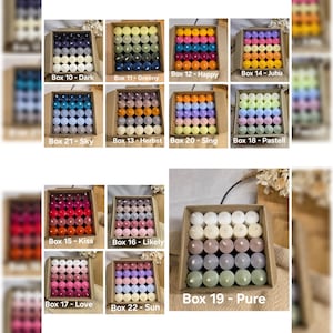 Könnte beinhalten: Eine Sammlung kleiner, farbiger Kugeln, angeordnet in Pappkartons. Jede Box ist mit einer Nummer und einem beschreibenden Wort wie "Dark", "Happy" und "Love" beschriftet. Die Kugeln variieren in der Farbe, einschließlich Blau-, Grün-, Rosa- und Orangetönen.