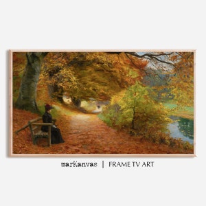 May include: An autumnal landscape painting showing a woman in a black dress and hat seated on a wooden bench. The scene depicts a path lined with trees in shades of yellow and orange, with a lake visible on the right. The text "markanvas | FRAME TV ART" is at the bottom.