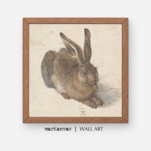 May include: A framed print of a brown hare, rendered in a detailed, realistic style. The artwork, set against a beige background, is enclosed in a wooden frame. The text "markanvas | WALL ART" is at the bottom.