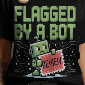 Könnte beinhalten: Schwarzes T-Shirt mit dem Text "FLAGGED BY A BOT" in pixeligen grünen Buchstaben. Ein pixeliger grüner Roboter hält ein rotes Schild mit "REVIEW". Das Design hat eine Retro-Videospiel-Ästhetik.