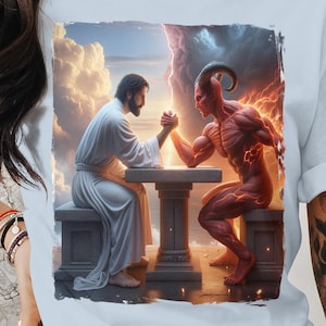 Könnte beinhalten: Ein hellblaues T-Shirt mit einem Grafikdruck eines roten Teufels und eines bärtigen Mannes, die Armdrücken spielen. Der Hintergrund ist ein bewölkter Himmel mit einem hellen Licht hinter dem Mann.