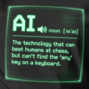 Op de afbeelding: Zwart T-shirt met een groene afbeelding van een computerscherm met het woord "AI" en een definitie. De definitie luidt: "De technologie die mensen kan verslaan met schaken, maar de 'any'-toets op een toetsenbord niet kan vinden."