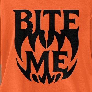 May include: Orange t-shirt with the words "BITE ME" in a black, stylized font. The design has a gothic, Halloween-themed aesthetic. The shirt is a short-sleeved, casual style.