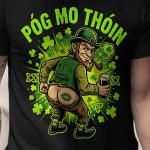 May include: Black t-shirt with a cartoon leprechaun graphic. The leprechaun is holding a beer and smoking a pipe, with a green shamrock design. The text "Póg mo thóin" is written in green above the leprechaun.