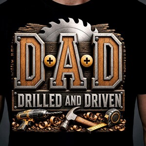 Puede incluir: Camiseta negra con un diseño gráfico que presenta la palabra "DAD" en una fuente de estilo madera, una hoja de sierra y la frase "DRILLED AND DRIVEN". Debajo, ilustraciones de herramientas como un taladro, un martillo y una cinta métrica.