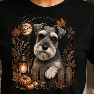 Puede incluir: Una camiseta negra con un estampado gráfico de un perro Schnauzer gris apoyando su pata en una valla de madera. La escena incluye una linterna brillante, calabazas, hojas de otoño y una luna llena, creando una detallada ilustración otoñal.
