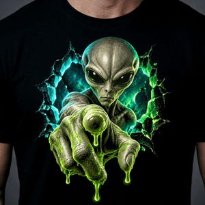 Puede incluir: Una camiseta negra con un estampado gráfico de un alienígena gris emergiendo de un portal verde brillante y agrietado. El alienígena extiende una mano texturizada cubierta de baba que parece gotear líquido verde sobre la tela.