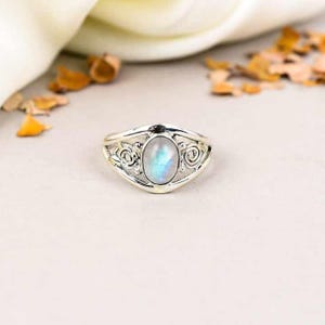 Puede incluir: Un anillo de plata con un delicado diseño de filigrana y una piedra ovalada de piedra lunar en el centro.