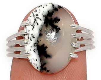 Può includere: Un anello in argento con una pietra preziosa di agata dendritica di forma ovale. La pietra presenta un aspetto diviso con una sezione bianca solida a sinistra e una sezione beige chiaro traslucida a destra, entrambe segnate da inclusioni nere.