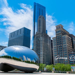 May include: A large, silver, bean-shaped sculpture reflects the surrounding cityscape, including tall buildings and a blue sky with white clouds. The sculpture is in a park setting with green trees and a paved area in the foreground. The text "Giovanny Valencia PHOTOGRAPHY" is visible in the lower right corner of the image.