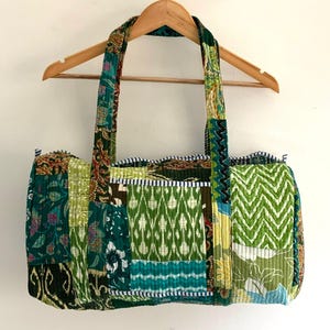 Puede incluir: Una bolsa de lona acolchada de patchwork verde y azul con ribete blanco. La bolsa tiene dos asas largas y está hecha de una variedad de telas.