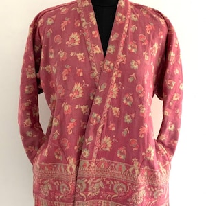 May include: A pink floral patterned shawl with a long fringe. The shawl has a shawl collar and long sleeves. The shawl is made of a soft, lightweight fabric.