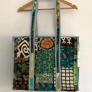 May include: A patchwork tote bag with green, brown and white fabric. The bag has a white and blue striped trim and two long straps.