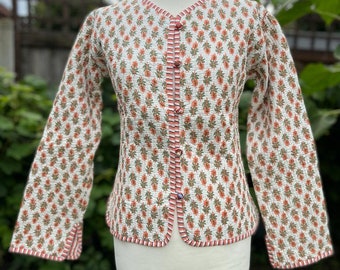 May include: A white quilted jacket with a floral print and red and white trim. The jacket has a button closure and long sleeves.