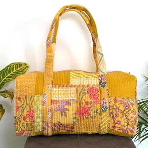 May include: A yellow patchwork tote bag with floral patterns and a quilted design. The bag has two long handles and a spacious interior.