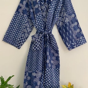 May include: A blue and white patterned robe with a tie waist. The robe is made of a patchwork design with various geometric and floral patterns. The robe is hanging on a wooden hanger.