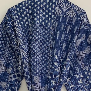 May include: A blue and white patterned robe with a belt. The robe features a patchwork design with various geometric and floral patterns. The fabric is a deep indigo blue with white accents, and the seams are stitched with white thread.