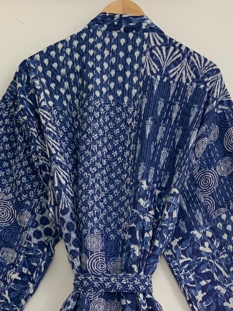 May include: A blue and white patterned robe with a belt. The robe features a patchwork design with various geometric and floral patterns. The fabric is a deep indigo blue with white accents, and the seams are stitched with white thread.