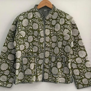 May include: A green quilted jacket with a white floral print and a mandarin collar. The jacket has a zip closure and two pockets.
