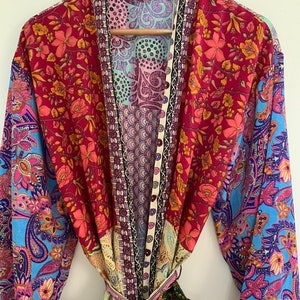 Może przedstawiać: Kolorowa, kwiatowa kimono z długimi rękawami i paskiem do wiązania. Kimono jest wykonane z miękkiej, jedwabistej tkaniny i występuje w różnych kolorach, w tym różowym, niebieskim, zielonym i czerwonym.