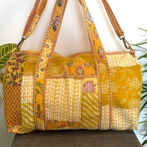 May include: A yellow patchwork tote bag with a floral print. The bag has two long straps and a zipper closure.