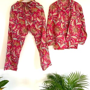 Puede incluir: Un conjunto de pijama rosa con estampado floral. La parte superior tiene un frente abotonado y mangas largas. Los pantalones tienen una cintura elástica.