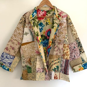 Può includere: Una giacca trapuntata patchwork con fodera a stampa floreale. La giacca è realizzata con diversi tessuti in tonalità beige, marrone e bianco. La fodera a stampa floreale è in tonalità rosa, blu e giallo.