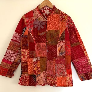 May include: A red, orange and brown patchwork quilted jacket with a mandarin collar and button fastening. The jacket features a variety of floral and geometric patterns.