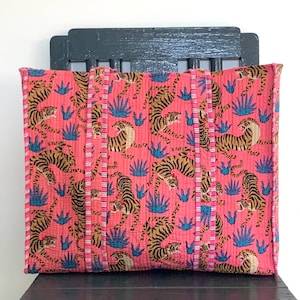 May include: A pink quilted tote bag with a tiger print and blue agave plants. The bag has brown straps and a white and pink trim.