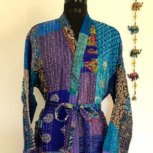May include: A blue and purple patchwork quilted robe with a sash tie. The robe is made from a variety of fabrics and has a unique, hand-stitched design.