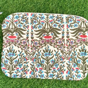 May include: A white zippered pouch with a floral pattern in shades of blue, green, and red. The pouch is made of fabric and has a quilted texture.