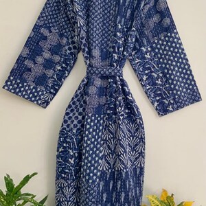 May include: A long, indigo blue robe with a patchwork design. The robe features a variety of patterns, including circles, dots, and leaf-like shapes, in white against the blue background. It has long sleeves and a matching belt.