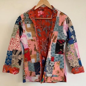 May include: A patchwork quilted jacket with a colourful floral and geometric print. The jacket has a long sleeve, a collar, and a front closure.