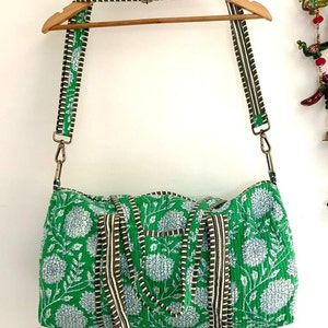May include: A green and white floral print duffel bag with brown and white striped straps. The bag has a zipper closure and a top handle.