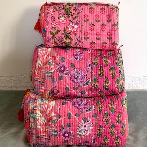 May include: Three pink quilted fabric zippered pouches with floral patterns. The pouches are stacked on top of each other.