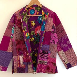 May include: A patchwork quilted jacket with a floral print in shades of pink, purple, and green. The jacket has a long sleeve and a button closure.