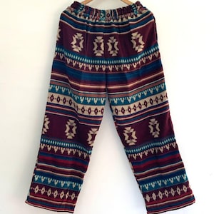 May include: Wide-leg trousers with a colourful geometric pattern in shades of burgundy, teal, cream, and brown. The trousers have an elastic waistband and a relaxed fit.