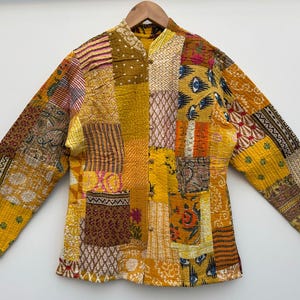 May include: A yellow, orange and brown patchwork jacket with a mandarin collar. The jacket is made of quilted fabric and has a unique, bohemian style.